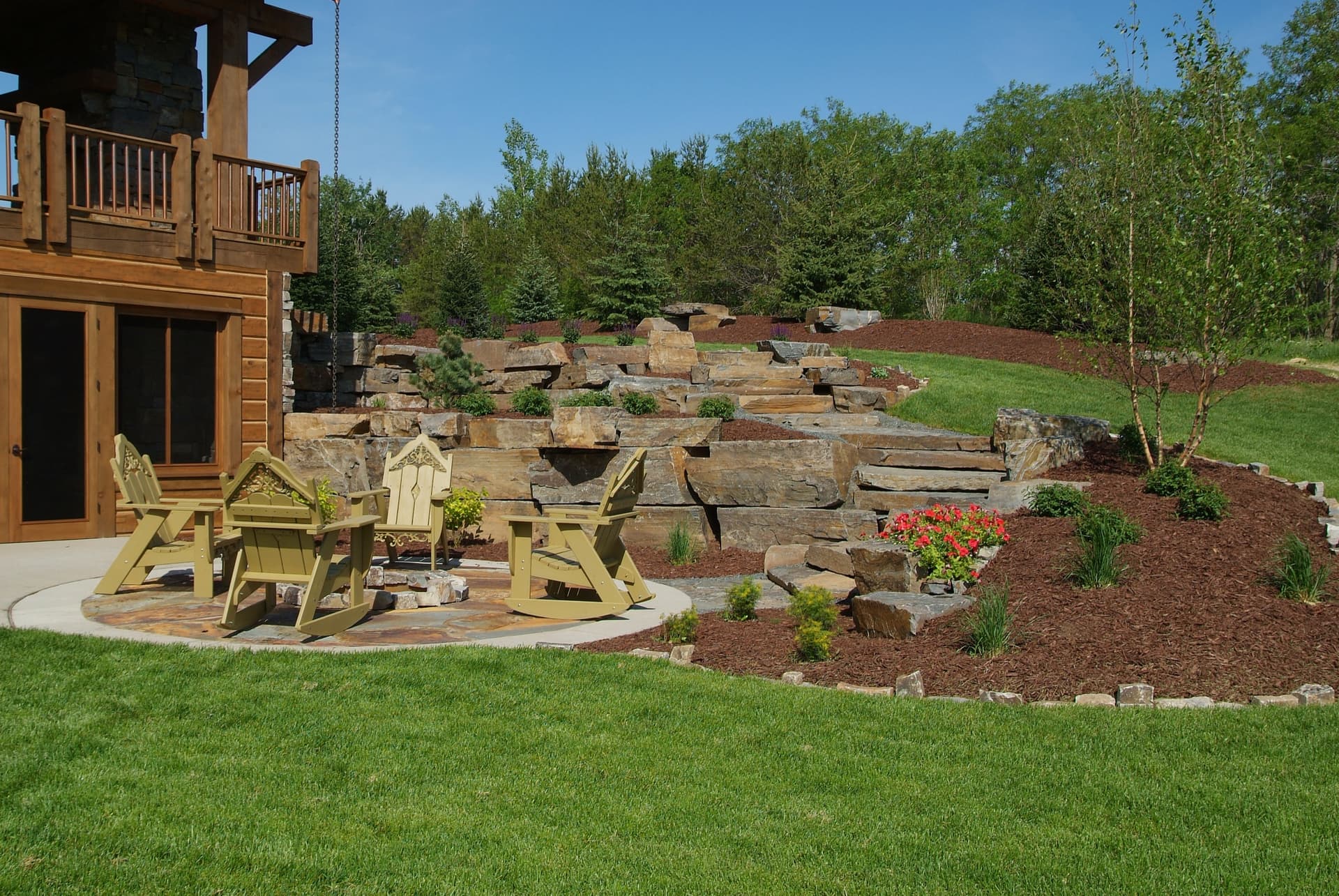 Massive stacked boulder retaining wall on hillside with Adirondack patio