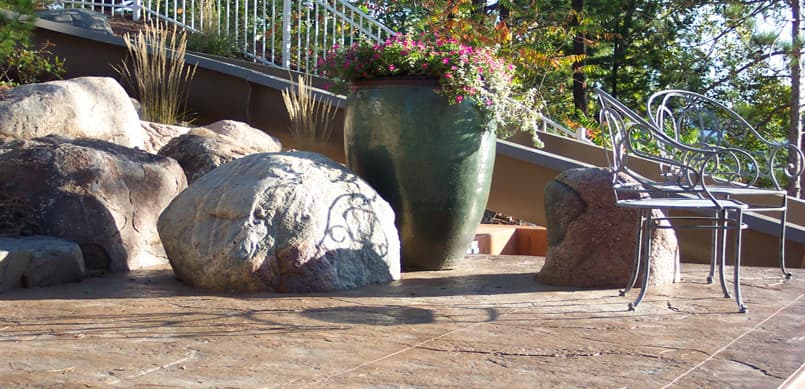 Patio with decorative boulders, large urn planter, and wrought iron bench