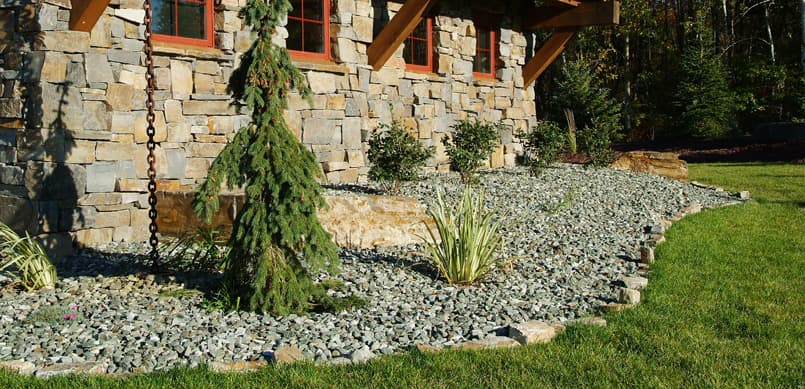 Decorative gravel and evergreen foundation planting on stone home
