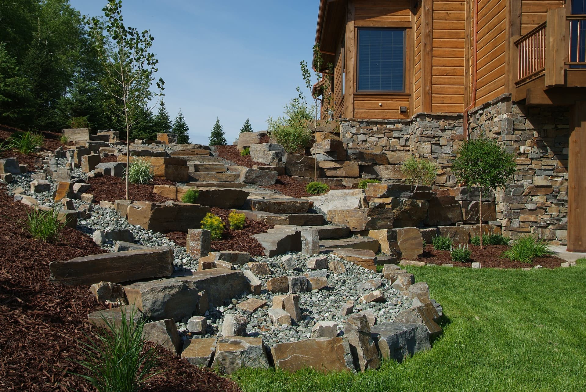 Tiered stone steps and boulder walls climbing to log home